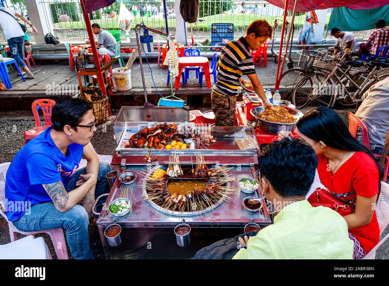 Eine Gruppe junger Menschen essen Essen aus einem Stall in der Innenstadt von Rangun, Yangon, Myanmar. Stockfoto
