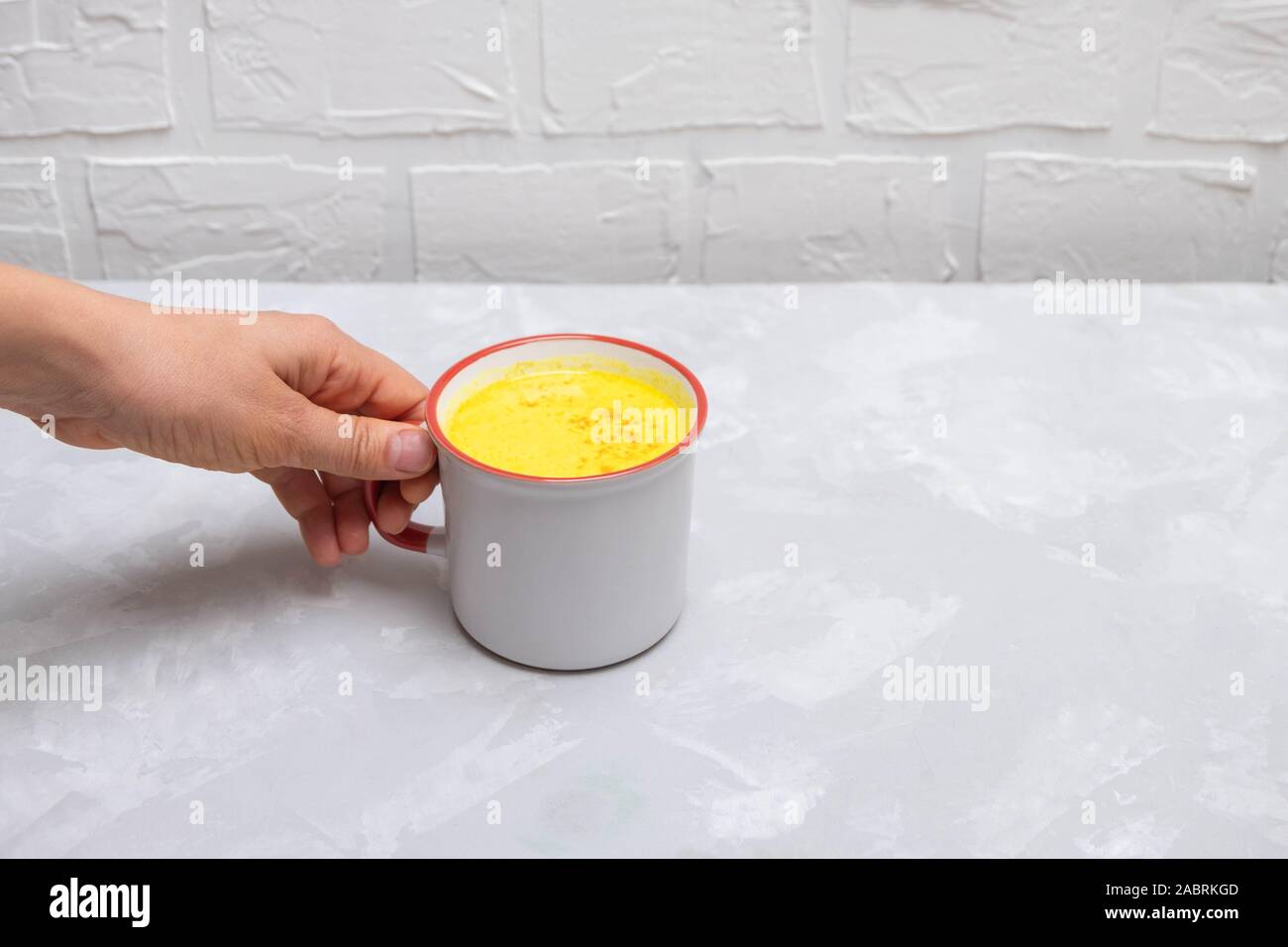 Frau hand Becher warmen anti-inflammatory trinken Gelbwurz golden Milch auf konkrete Küche Hintergrund. Stockfoto