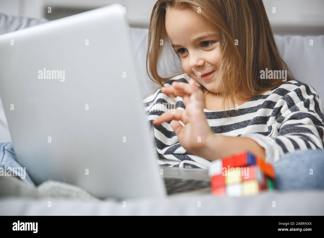 Kleines Kind Mädchen drinnen sitzen auf der Coach surfen Laptop Webseiten mit Spielzeug schließen Lächeln - Bis Stockfoto