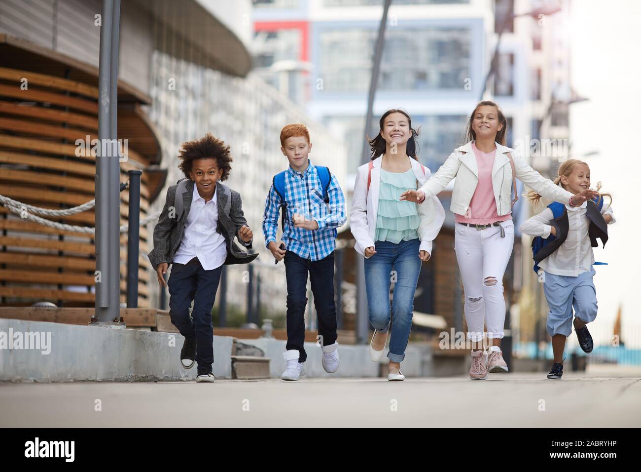 Gruppe von multiethnischen Schule Kinder zusammen die Straße entlang laufen nach der Schule Stockfoto