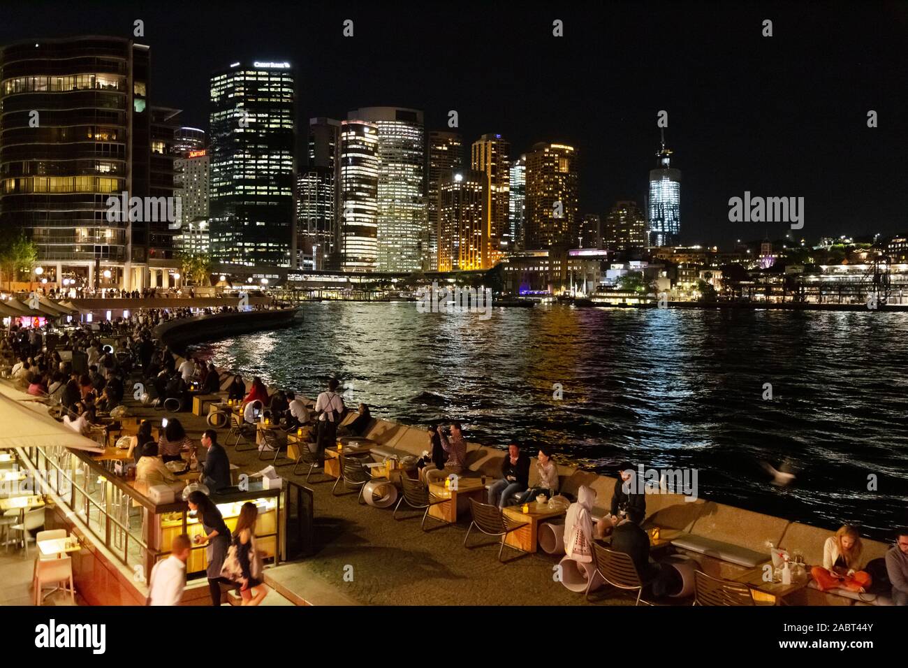 Sydney Nacht; Sydney Harbour und Circular Quay in der Nacht, mit Wolkenkratzern und Menschen essen in der Opera Bar im Frühling, Sydney, Australien Stockfoto