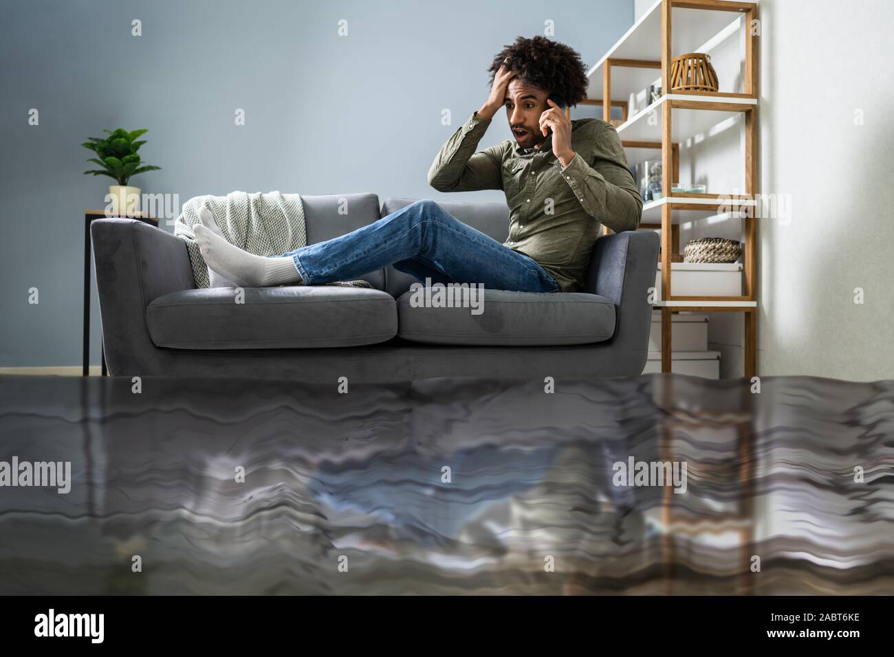 Überschwemmt von Wasser Leckage Vor Mann sitzt auf einem Sofa zu Klempner Stockfoto