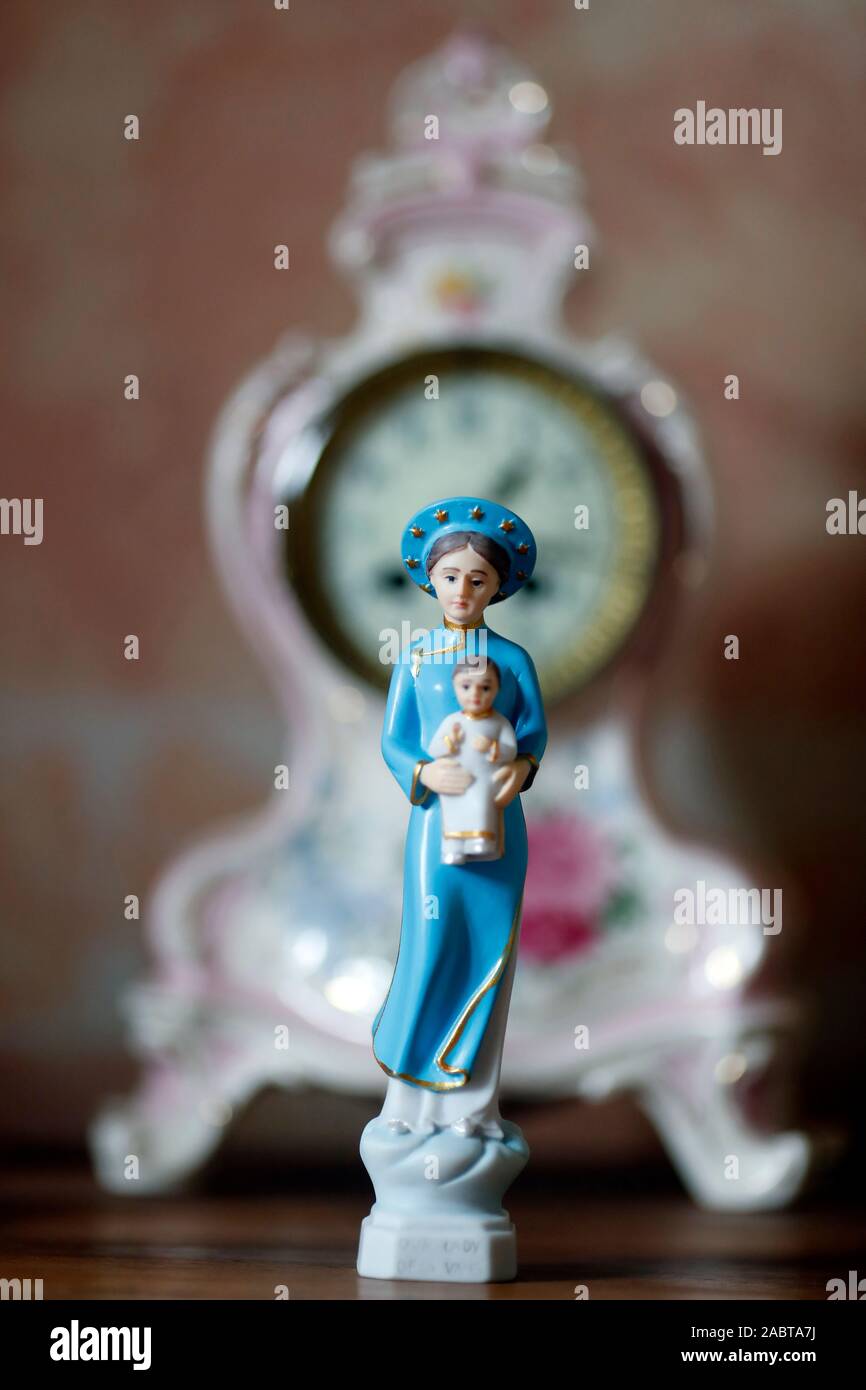 Jungfrau Maria und das Kind Jesu Christi. Unsere Liebe Frau von La Vang. Figur auf einem Tisch vor einer Uhr. Frankreich. Stockfoto