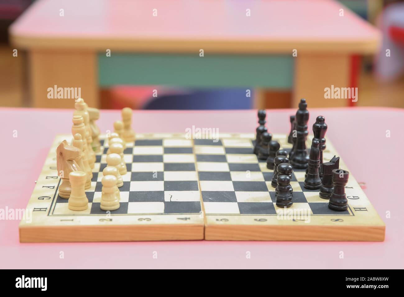 Holz- Schachfiguren auf dem Schachbrett. Intellektuelles Spiel. Holz- Schachfiguren und Schachuhr auf einem rosa Hintergrund. Stockfoto