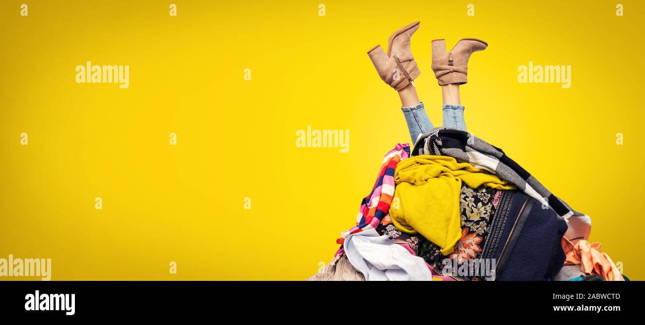 Frau Beine aus der Kleidung Stapel auf gelben Hintergrund mit Kopie Raum Stockfoto
