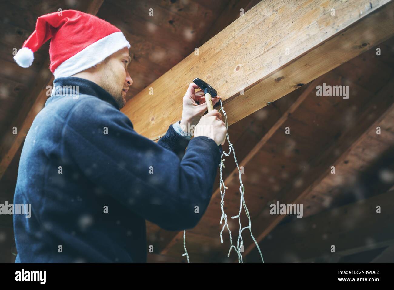 Mann mit Santa Hut verzieren Haus Außenbereich Carport mit Weihnachten Lichterkette Stockfoto