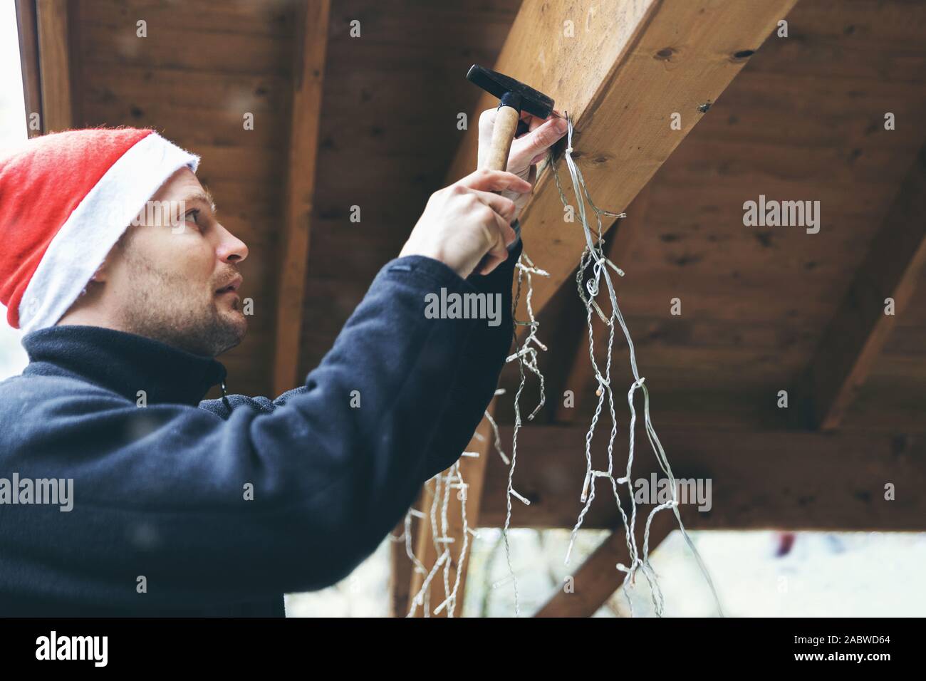 Mann mit Santa Hut verzieren Haus Außenbereich Carport. Installation der Weihnachtsbeleuchtung Stockfoto