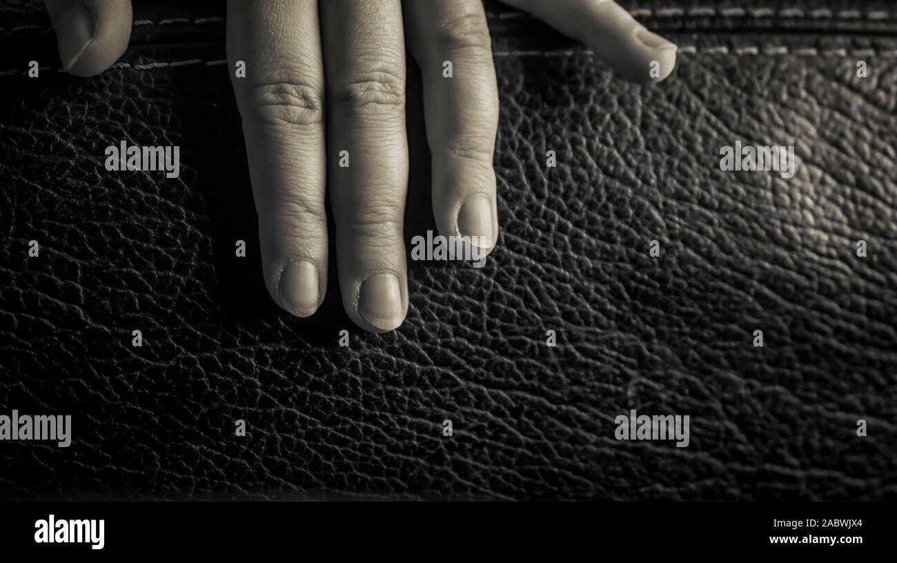 Eine Nahaufnahme der Finger einer Frau auf einem Ledersessel in Schwarz und Weiß Stockfoto