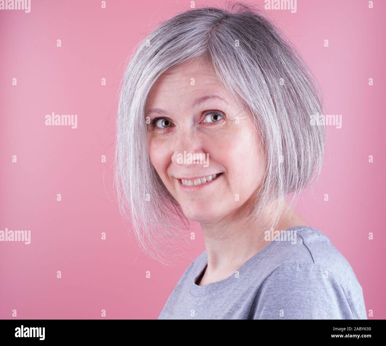 Close-up Porträt einer Frau, die in den frühen fünfziger Jahren mit grauem Haar, rosa Hintergrund Stockfoto