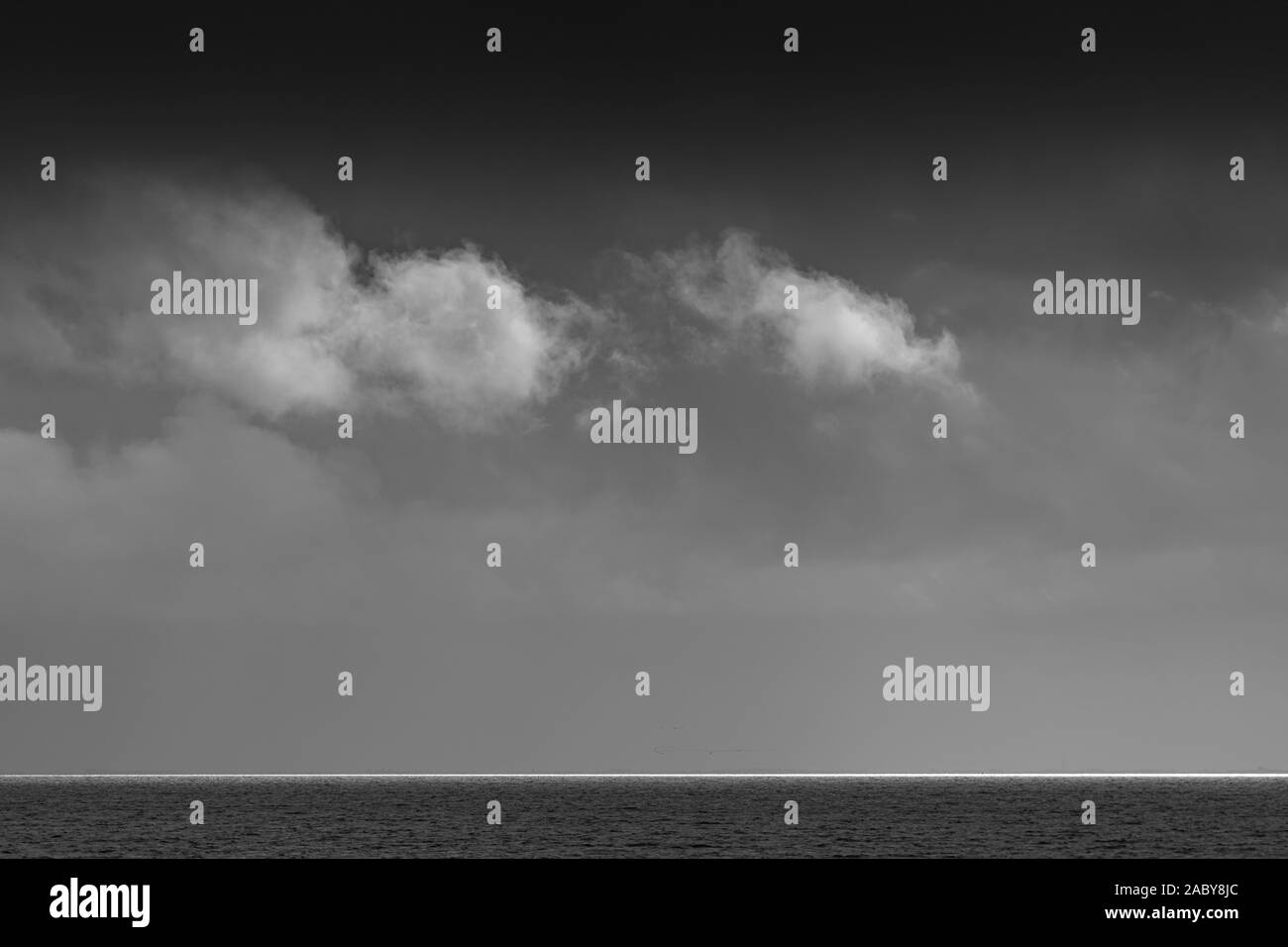 Weiße Wolken über das Wattenmeer mit einem Streifen von weißem Licht am Horizont in Schwarz und Weiß Stockfoto