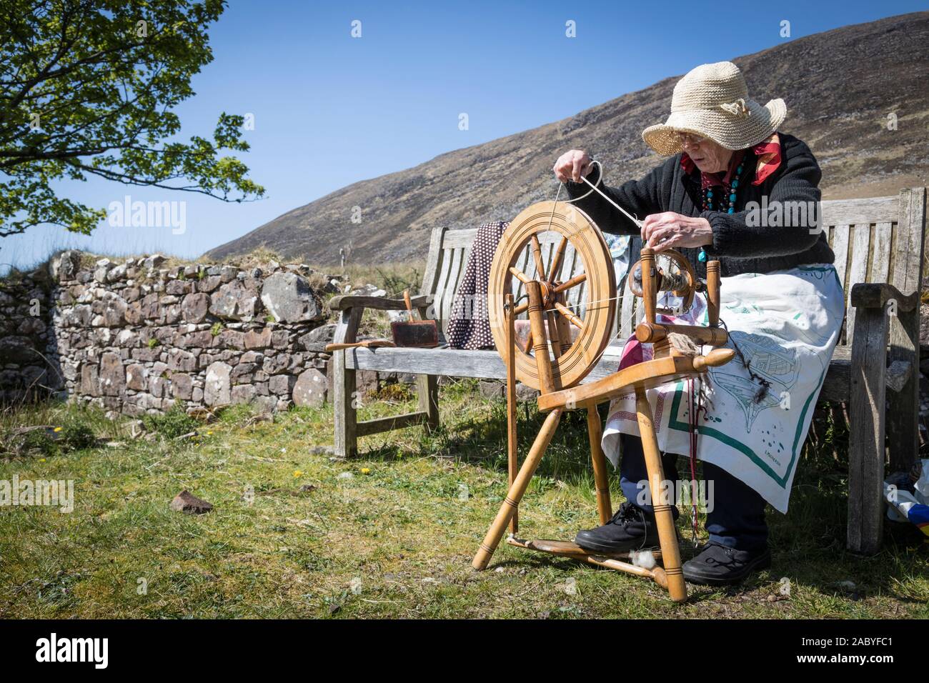 Eine ältere Frau trägt einen Hut gegen die Sonne dreht Schafwolle mit einer  manuellen Spinnrad, Sangerhausen, Schottland Stockfotografie - Alamy