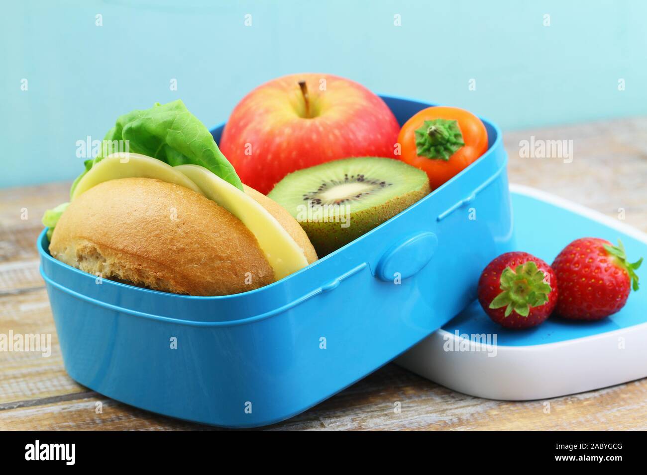 Gesunde Brotdose mit Cheese Roll mit Salat und Tomaten und frischem Obst: Apfel, Kiwi und Erdbeeren Stockfoto