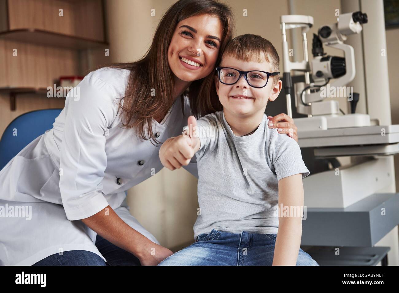 Junge zeigt Daumen hoch. Weibliche Auge Doktor sitzt mit dem Kind nach