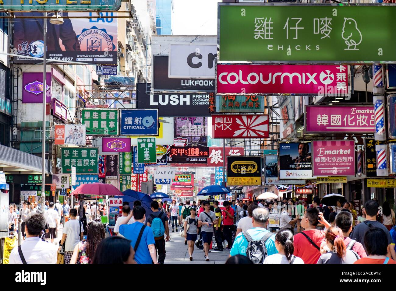 Menschenmassen laufen durch eine geschäftige Straße in Hongkong, umgeben von farbenfrohen Schildern und Anzeigen. Stockfoto