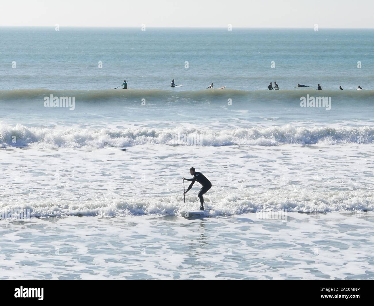 Winter surfen am Selsey Strand im Februar 2019 mit einem Surfer Paddeln in die Wellen stehend auf seinem Surfbrett in den flachen seafoam Stockfoto