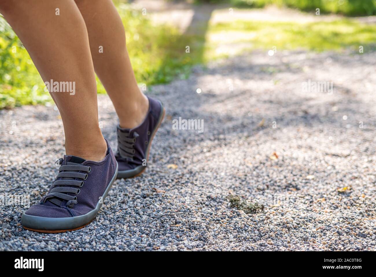 Weibliche Beine in Turnschuhen auf den Spuren der Kies im Sommer, auf einem unscharfen Hintergrund grün. Konzept eines aktiven Lebensstils. Stockfoto