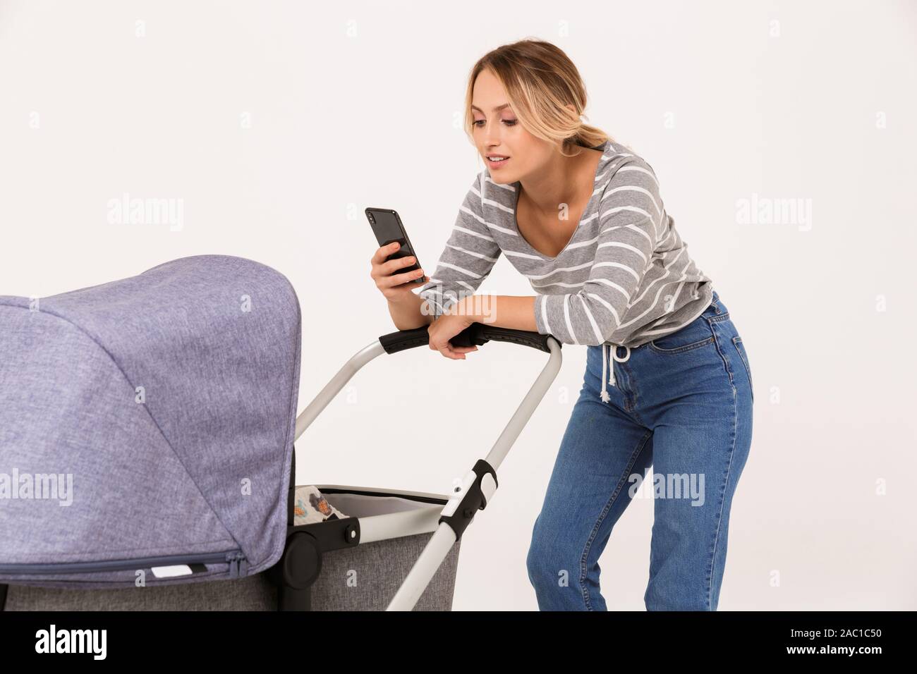 Schöne junge Frau mit einem Baby Kinderwagen auf weißem Hintergrund, mit Handy Stockfoto