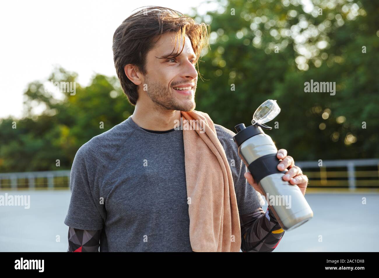 Foto von Stattlichen glücklicher Mann in Sportkleidung Trinkwasser und lächelnd, während sie auf dem Spielplatz im Freien arbeiten Stockfoto