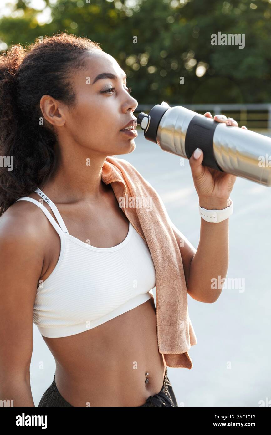 Foto der afrikanischen amerikanischen süsse Frau mit Handtuch Trinkwasser aus der Flasche, während sie auf dem Spielplatz im Freien arbeiten Stockfoto