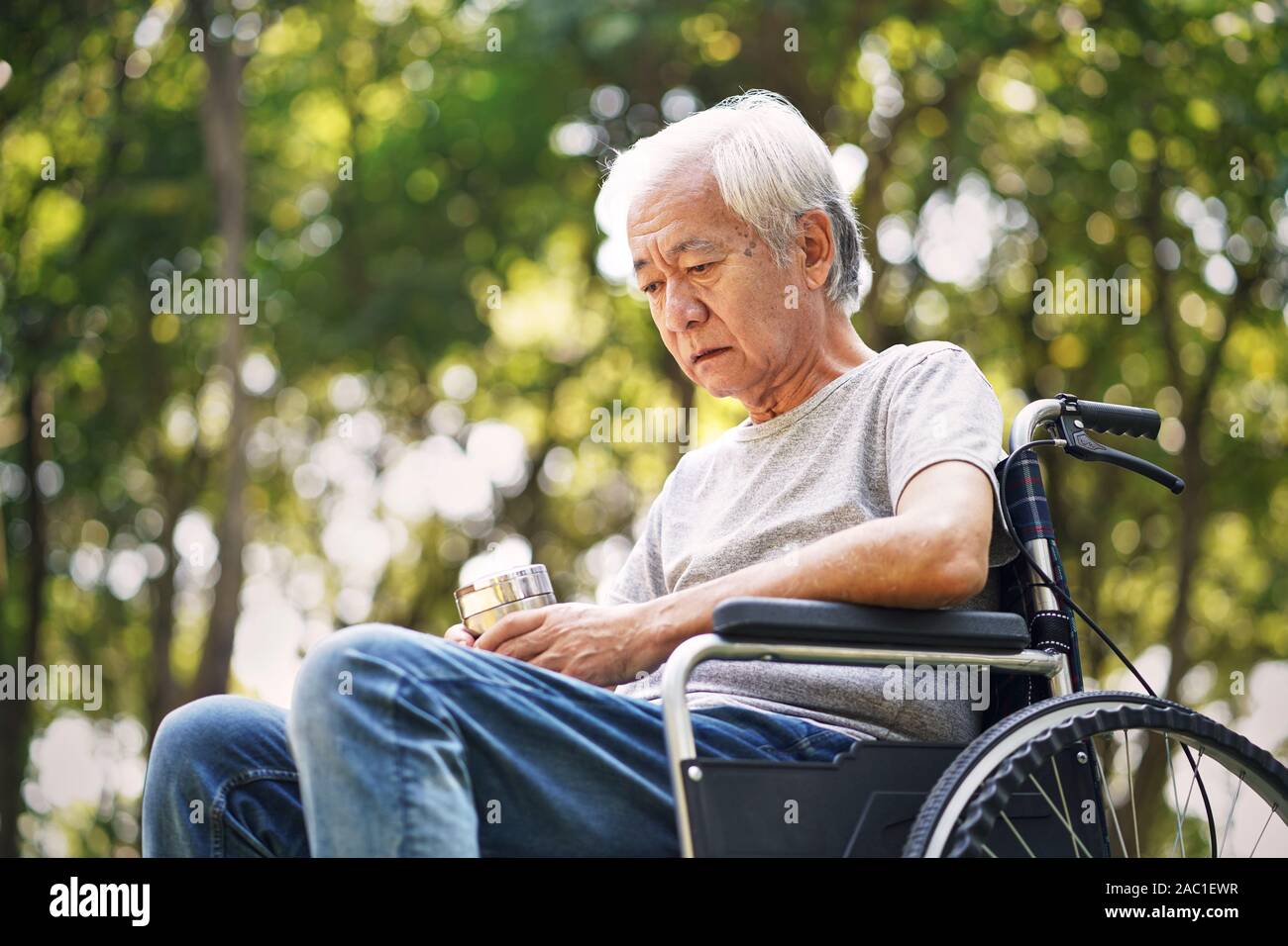 Asiatische alte Mann sitzt im Rollstuhl, mit dem Kopf nach unten schaut traurig und deprimiert Stockfoto