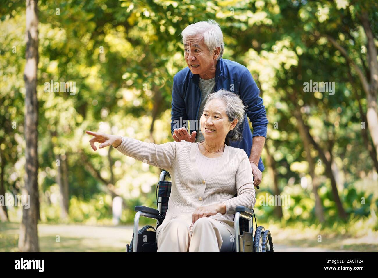Senior asiatischer Mann Wandern im Park mit Rollstuhl gefesselt Frau Stockfoto