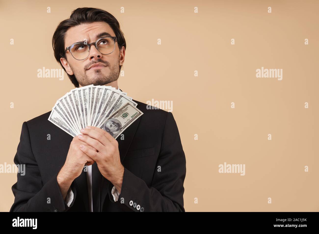 Porträt einer stattlichen nachdenkliche junge Unternehmer tragen Anzug stehen über beigen Hintergrund isoliert, mit Geld Banknoten Stockfoto