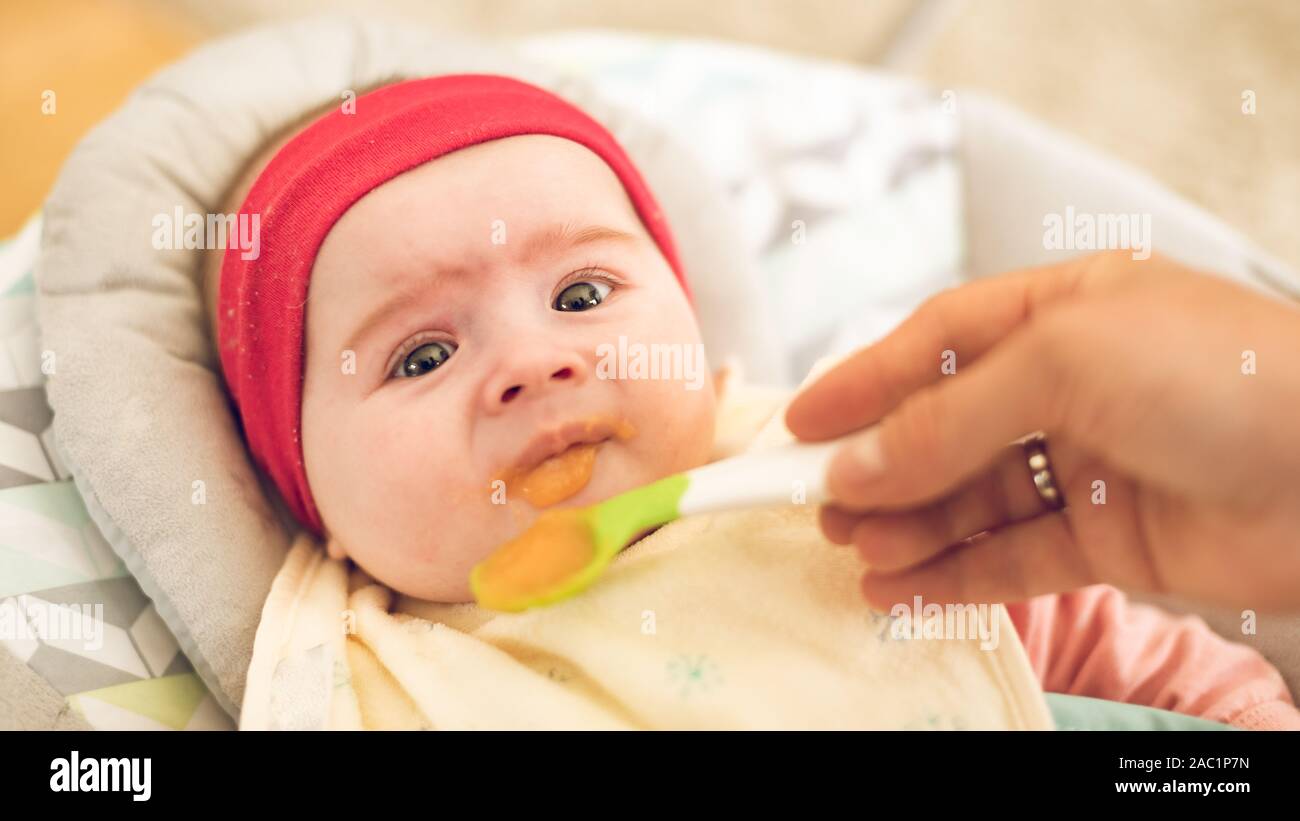 Mutter Fütterung hungrigen fünf Monate alten lustig Baby mit fester Nahrung. Stockfoto