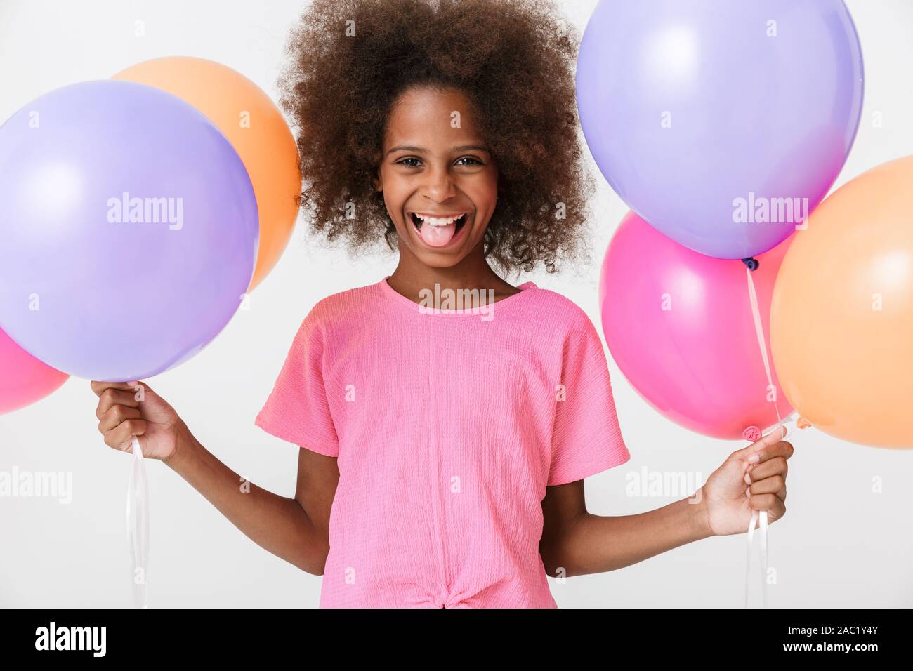 Fröhliche kleine afrikanische Mädchen mit rosa Bluse auf weißem Hintergrund, die Flosse mit Luftballons, ihr die Zunge heraus Stockfoto