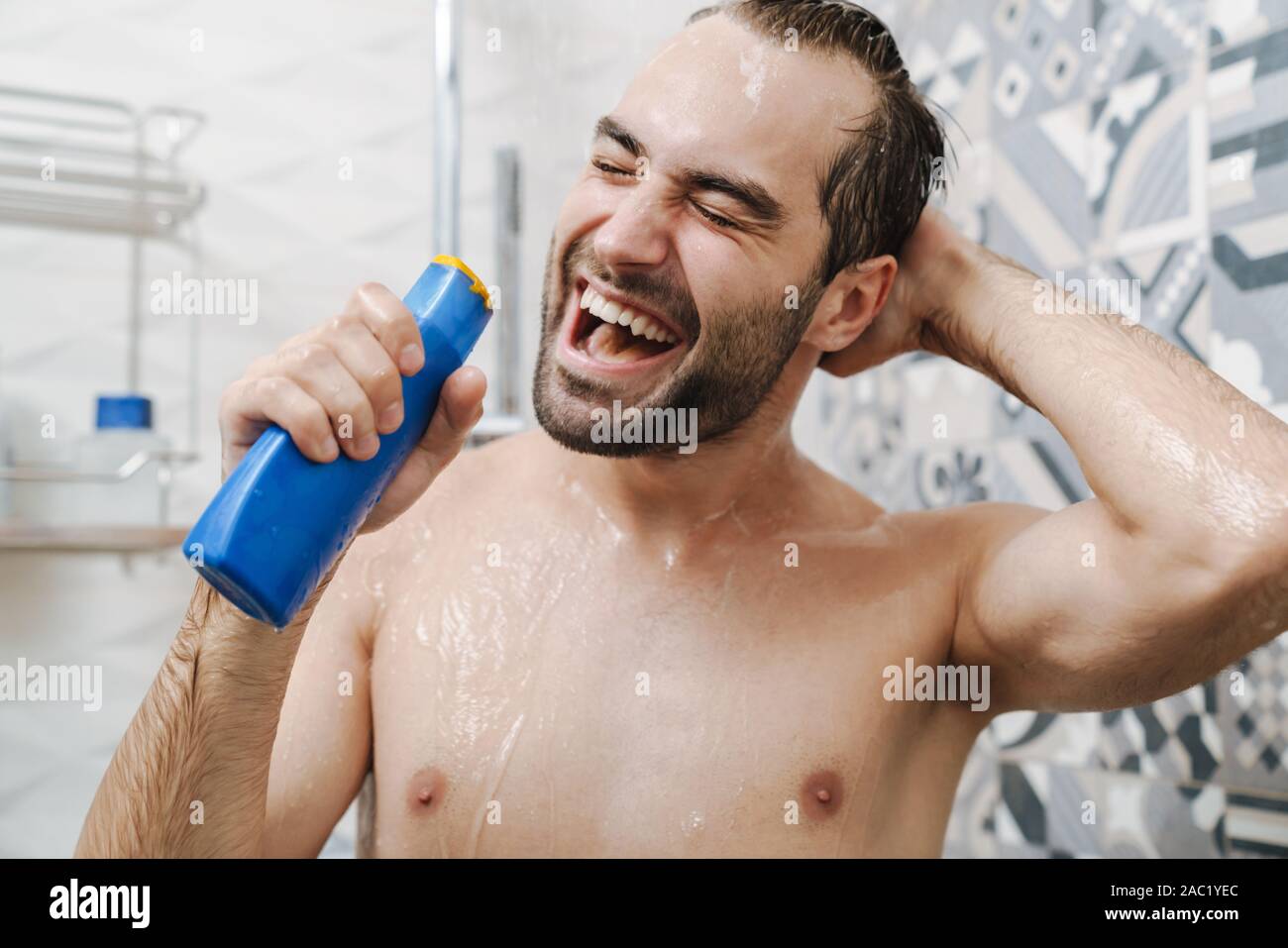 Attraktive junge fröhliche Mann singen beim Waschen unter der Dusche, Shampoo Flasche Stockfoto
