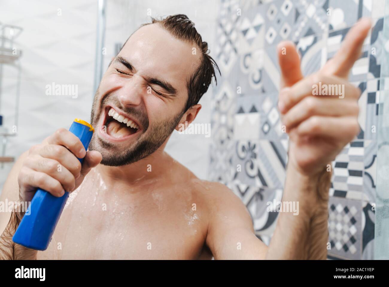 Attraktive junge fröhliche Mann singen beim Waschen unter der Dusche, Shampoo Flasche Stockfoto