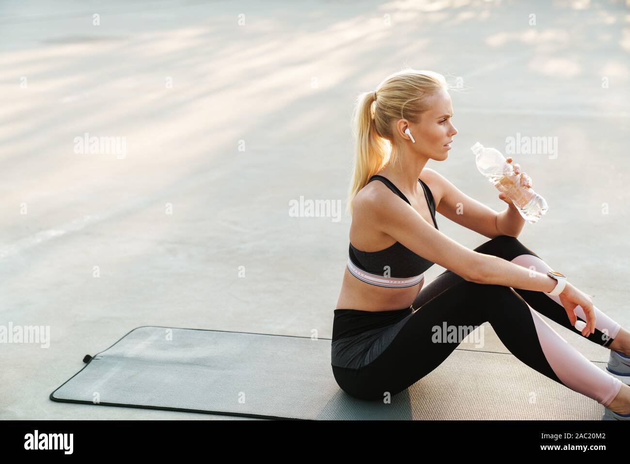 Bild des fokussierten Sportlerin im Trainingsanzug Trinkwasser während des Trainings auf Fitness Matte im Freien Stockfoto