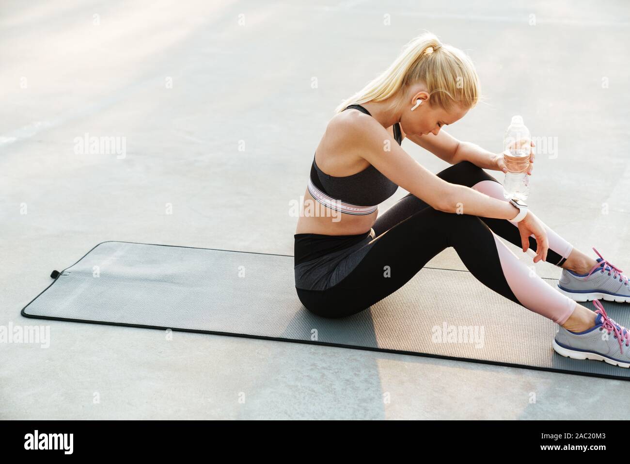 Bild des athletischen Sportlerin im Trainingsanzug Trinkwasser während des Trainings auf Fitness Matte im Freien Stockfoto