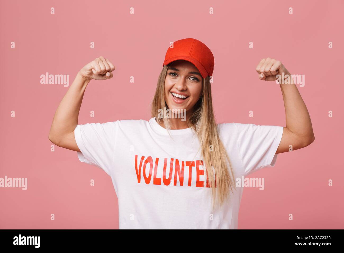 Glückliche junge Freiwillige stehendes Mädchen über rosa Hintergrund isoliert, flexing Biceps Stockfoto