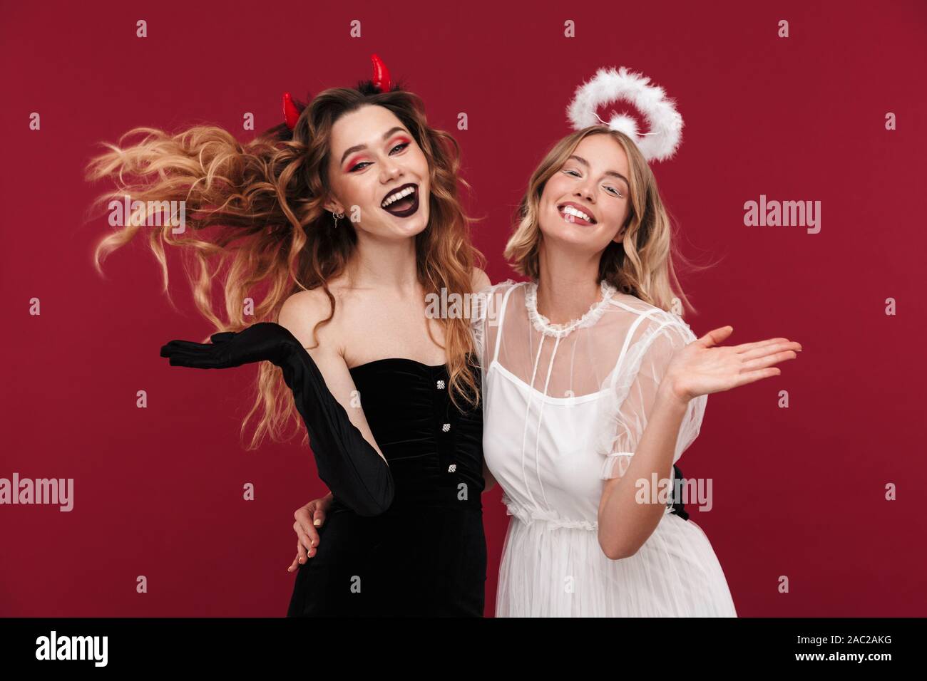 Bild der glücklichen positive Frauen Dämon und Engel in Karneval Kostüme über rote Wand Hintergrund isoliert. Stockfoto