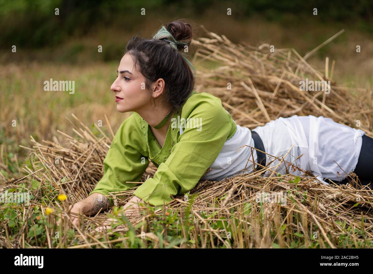 Mädchen liegt in einem Weizenfeld und auf Heu trockenes Gras posiert, Sommersaison. Entspannen und genießen Sie die Natur. Junge Frau im Feld posieren. Einstellung zurücksetzen Stockfoto