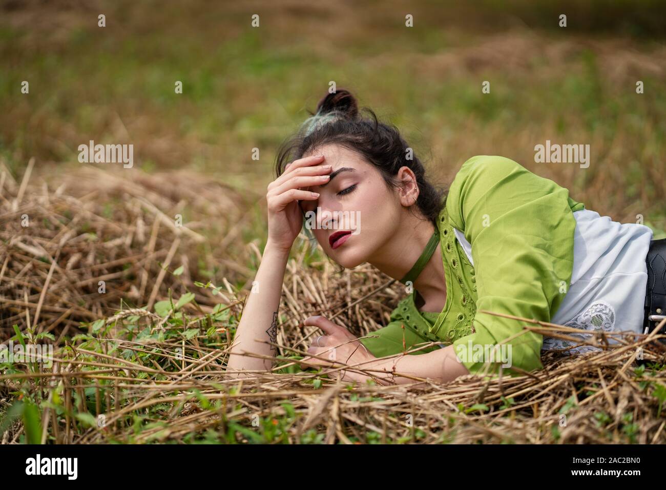 Mädchen liegt in einem Weizenfeld und auf Heu trockenes Gras posiert, Sommersaison. Entspannung in der Natur. Junge Frau im Feld posieren. Einstellung zurücksetzen Stockfoto