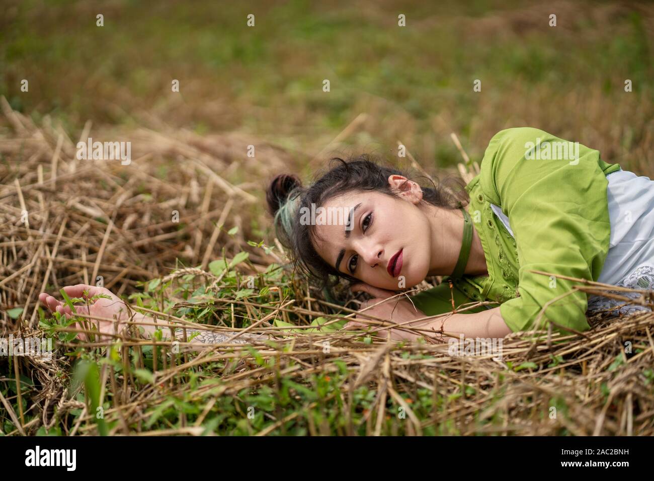 Mädchen liegt in einem Weizenfeld und auf Heu trockenes Gras posiert, Sommersaison. Entspannung in der Natur. Junge Frau im Feld posieren. Einstellung zurücksetzen Stockfoto