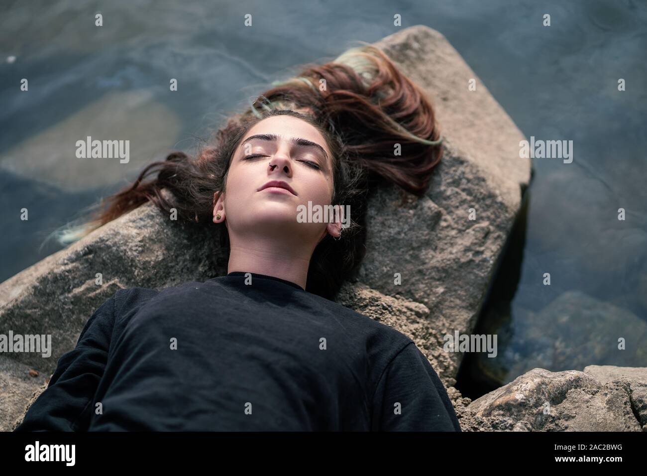 Mädchen liegt und Träumen auf Felsen in der Nähe des Flusses. Entspannung in der Natur. Junge Frau schlafen auf Stein über Wasser. Einstellung zurücksetzen Stockfoto