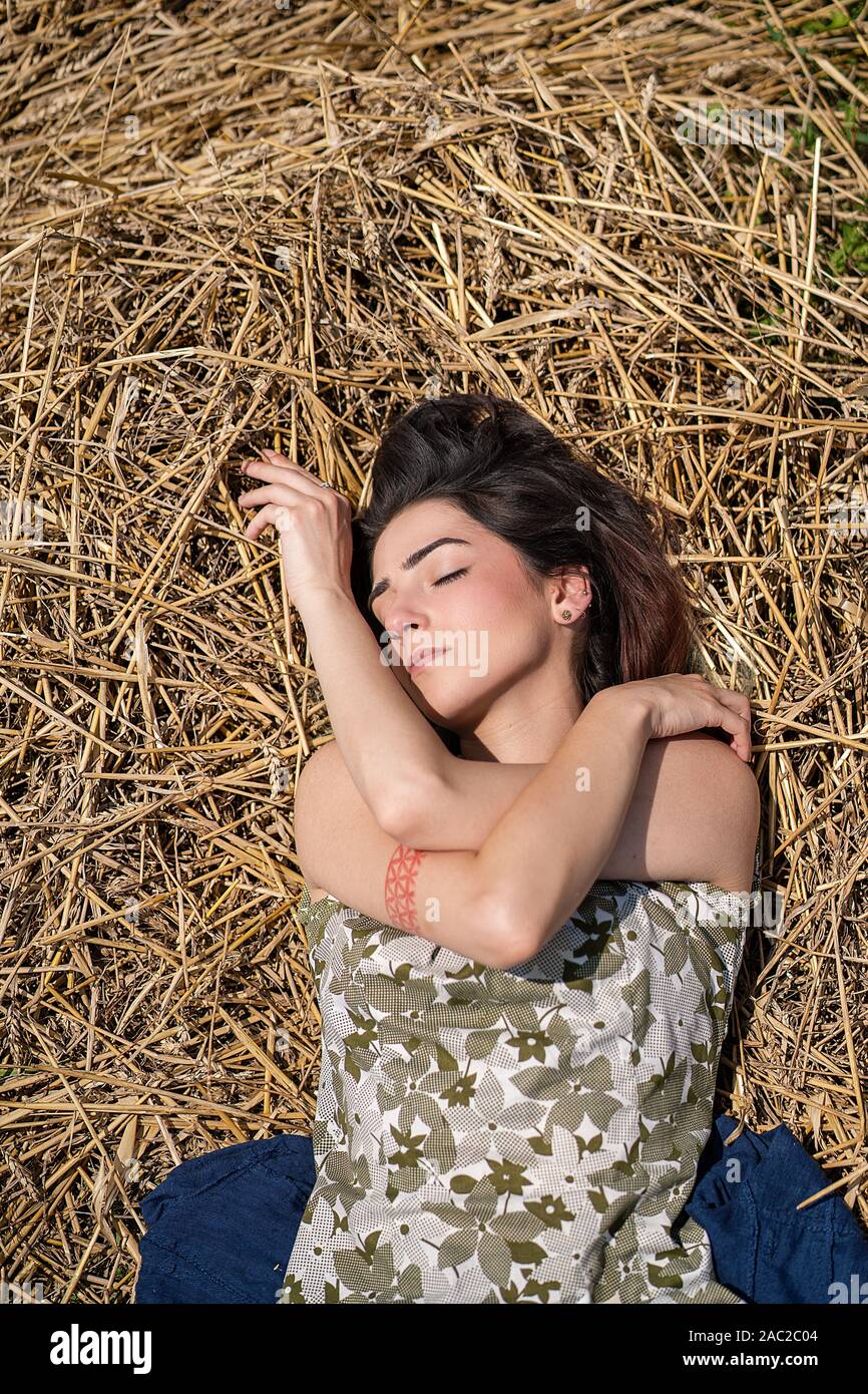 Mädchen liegt in einem Weizenfeld und auf Heu trockenes Gras posiert, Sommersaison. Entspannen und genießen Sie die Natur. Junge Frau im Feld posieren. Einstellung zurücksetzen Stockfoto