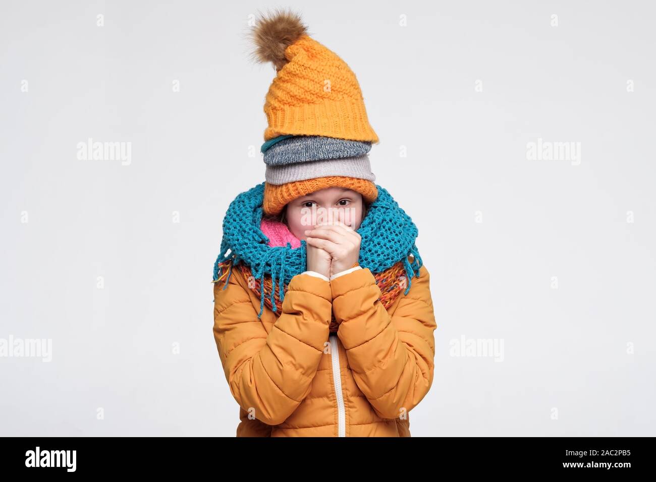 Lustig Junge kaukasier Frau zitternd vor Kälte tragen mehrere warme Winter Mützen und Schals. Studio shot Stockfoto