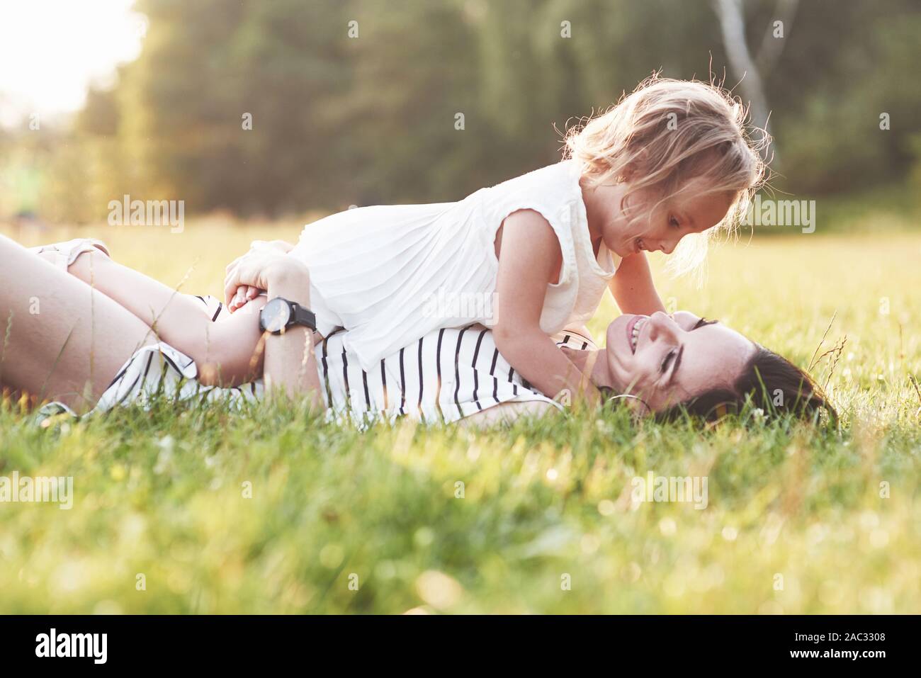 Legen Sie sich auf das Gras. Schönes Portrait von Mädchen und ihre Tochter umarmen sich außerhalb Stockfoto