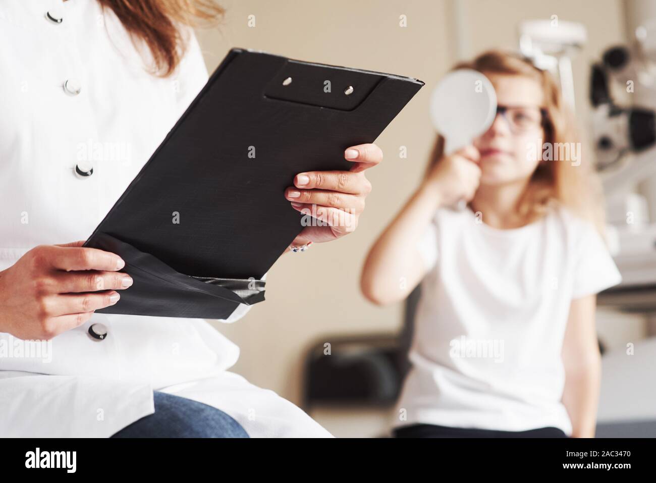 Auge Gesundheit Konzeption. Frau mit Unterlagen prüft die Sehschärfe des kleinen Mädchens Stockfoto