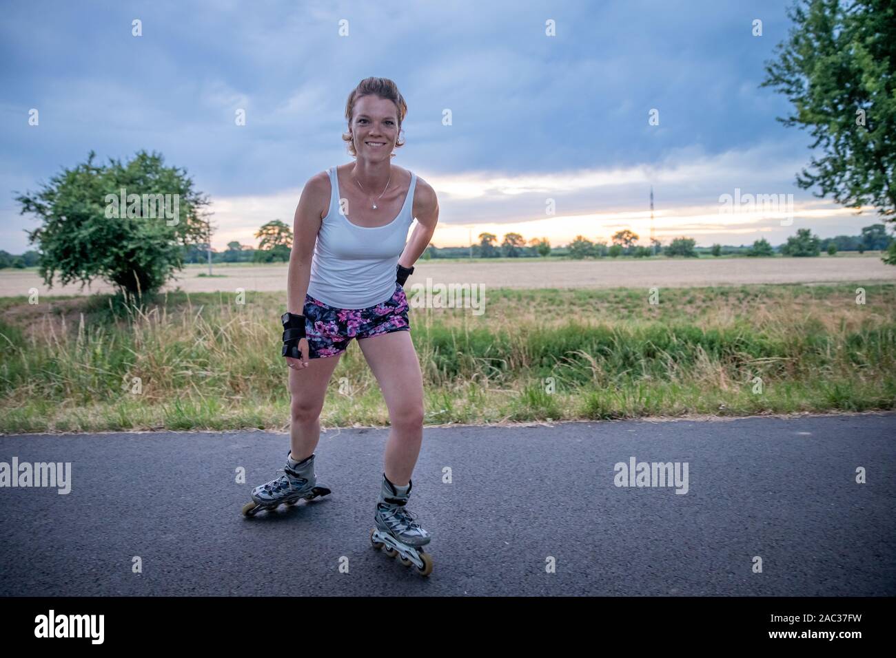 Junge attraktive Frau reitet Rollschuhe in der Landschaft im Sommer Stockfoto