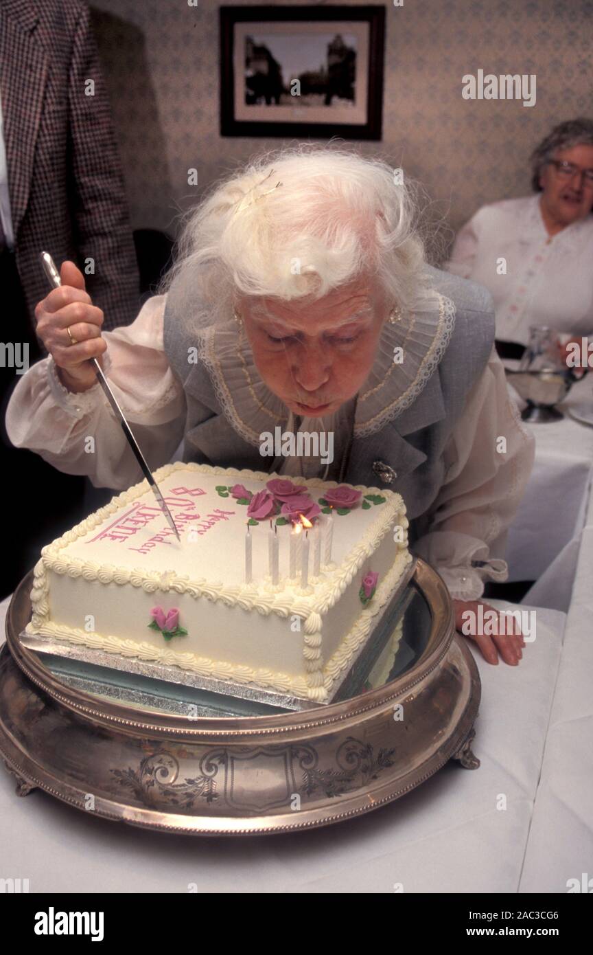 Lady ausblasen Kerzen auf Ihrem 80. Geburtstag Kuchen Stockfoto