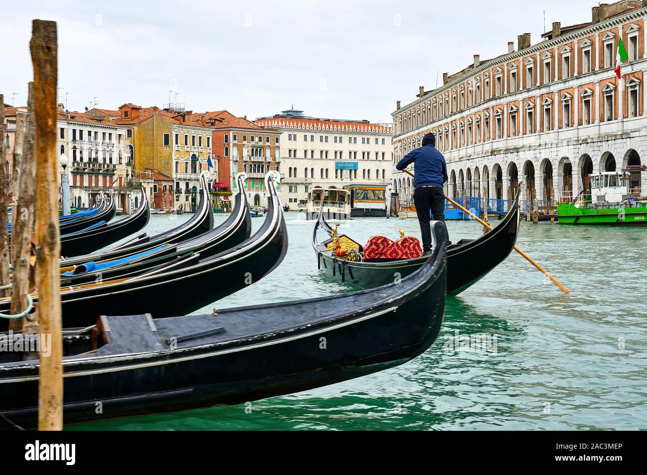 Ein gondoliere Lenkung seine Gondel Vergangenheit eine Linie der angelegten Boote am Grand Canal in Venedig Italien Stockfoto