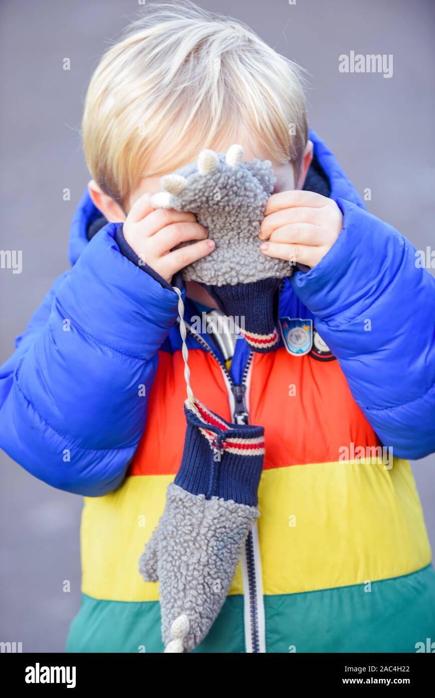 Ein- und Ausblenden der Junge außerhalb spielt in Outdoor Bekleidung ist er für Gesicht und verstecken, während sie in die Kamera schaut suchen Stockfoto