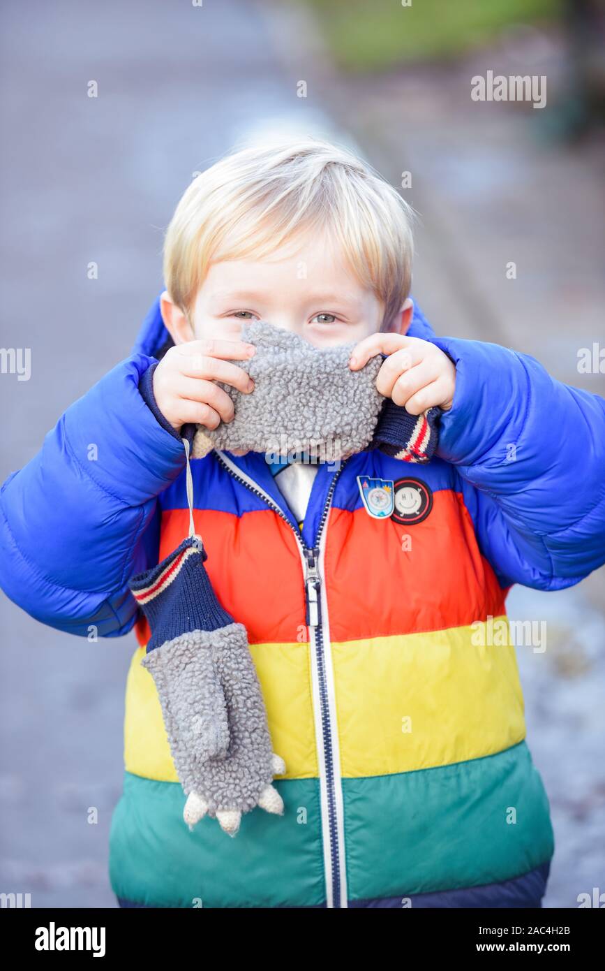 Ein- und Ausblenden der Junge außerhalb spielt in Outdoor Bekleidung ist er für Gesicht und verstecken, während sie in die Kamera schaut suchen Stockfoto