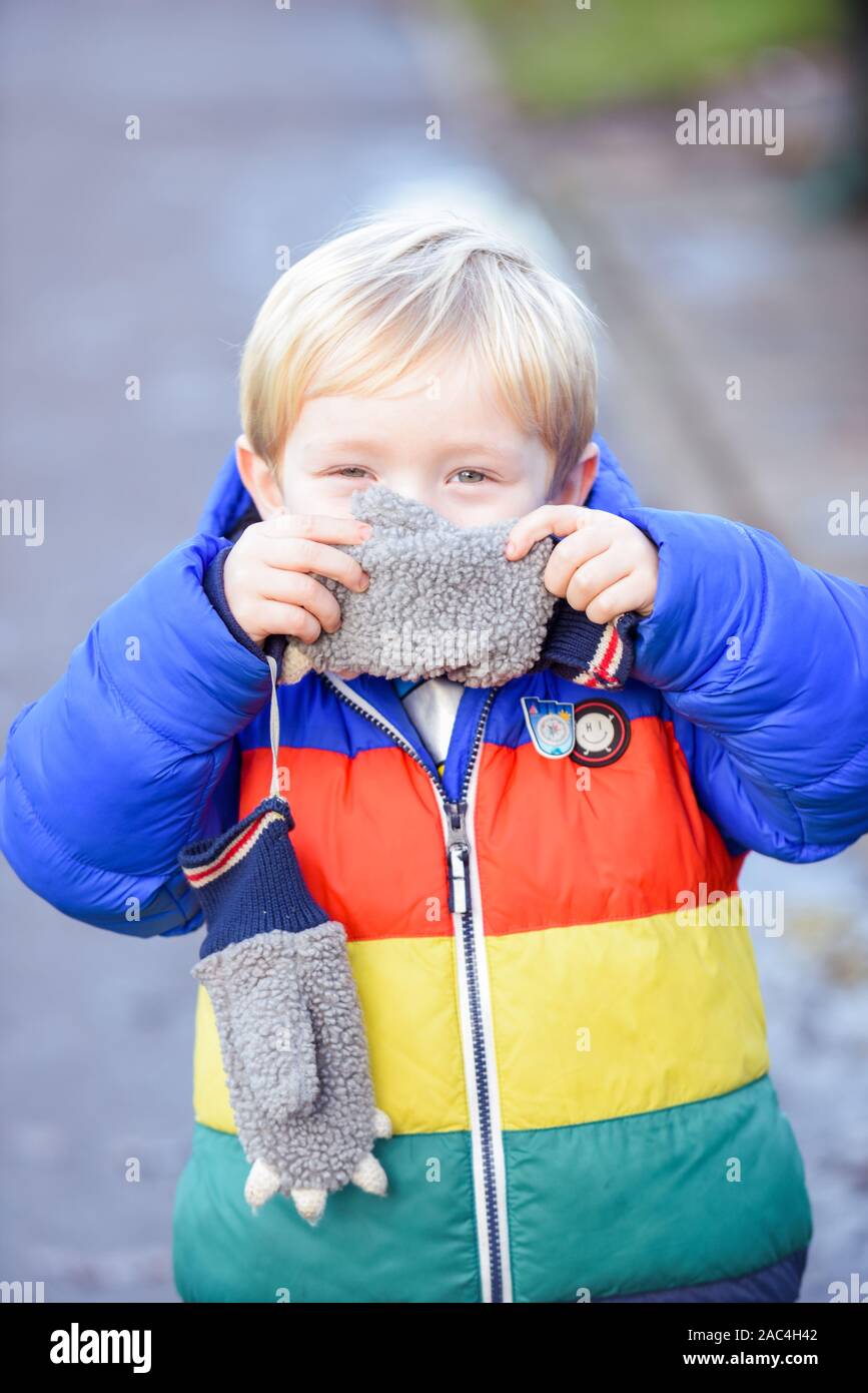 Ein- und Ausblenden der Junge außerhalb spielt in Outdoor Bekleidung ist er für Gesicht und verstecken, während sie in die Kamera schaut suchen Stockfoto