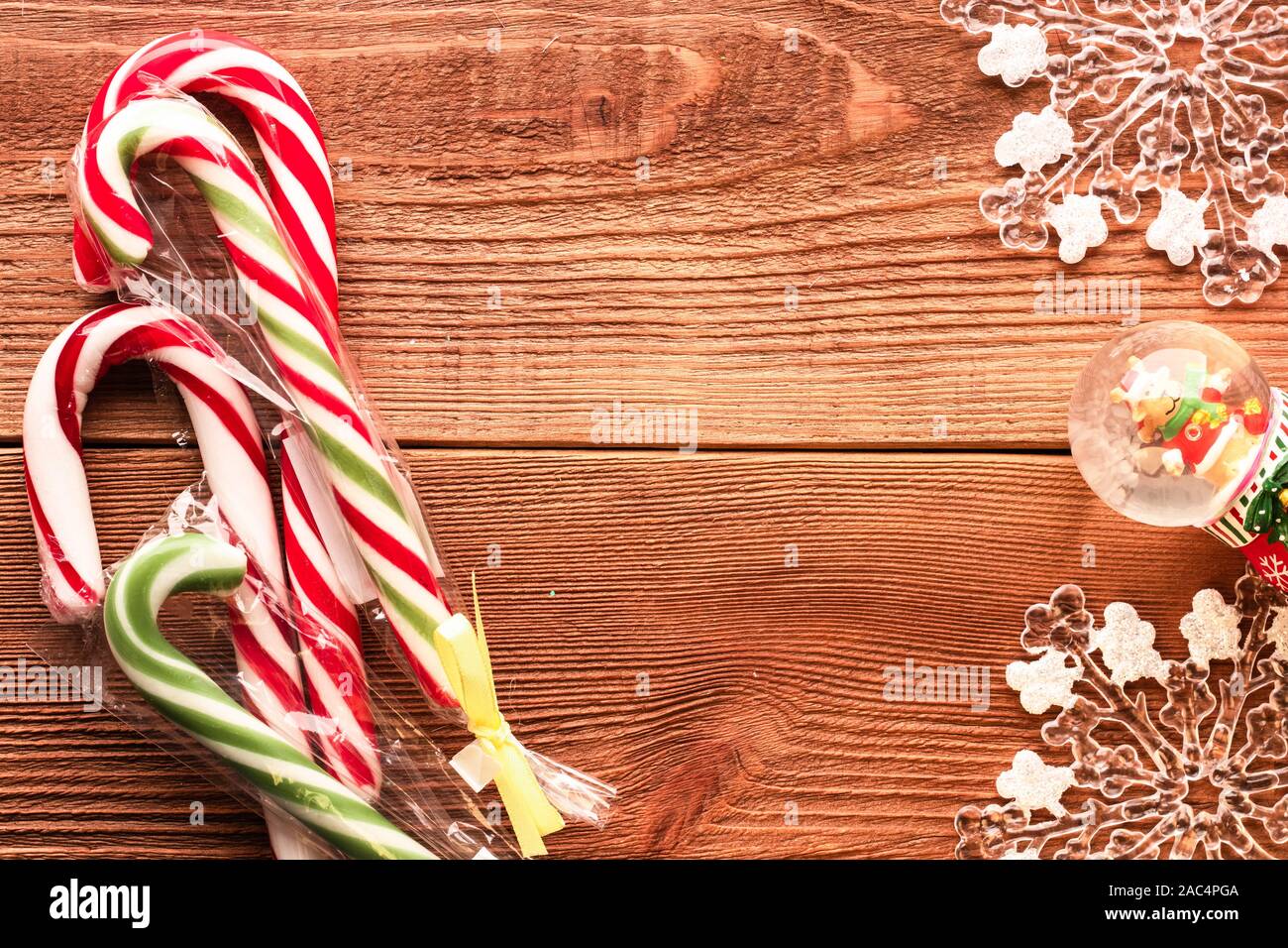 Frohe Weihnachten. Ansicht von oben Foto von Bunte rote und grüne Süßigkeiten Stöcke, große Schneeflocken und kleine Schneekugel mit wenig Rehe innen auf natürliche Braun Stockfoto