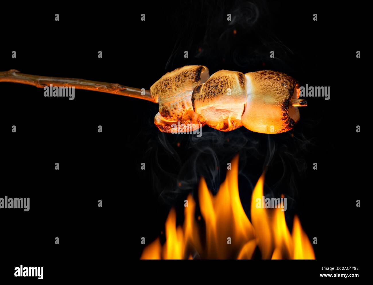 Marshmallows auf Holzstab Rösten über Feuer flammen Stockfoto
